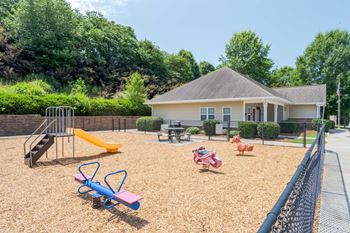 A playground with a slide, swings, and a seesaw in front of a house